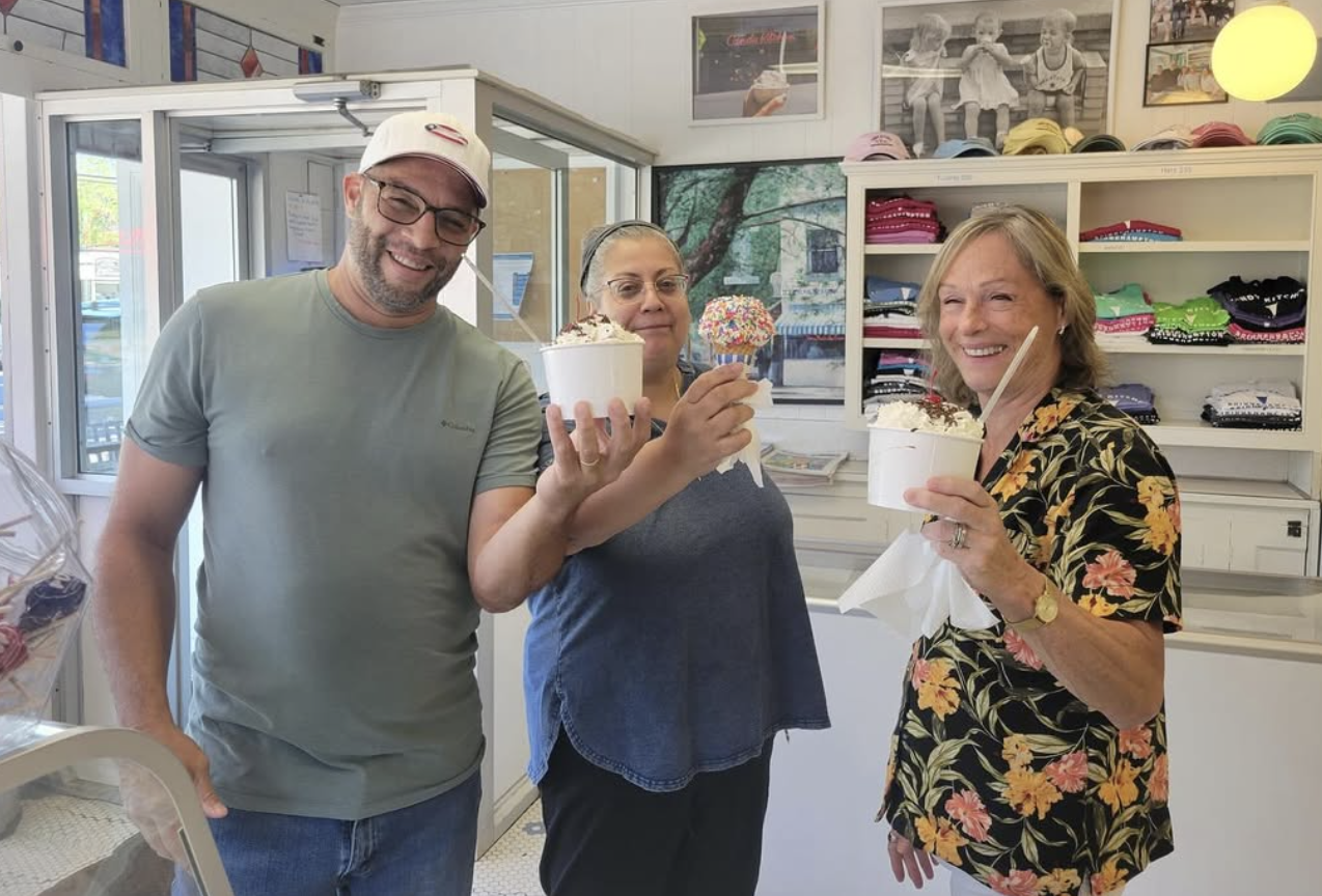 Three smiling customers holding ice cream cups and a sprinkle-coated cone at the Candy Kitchen counter