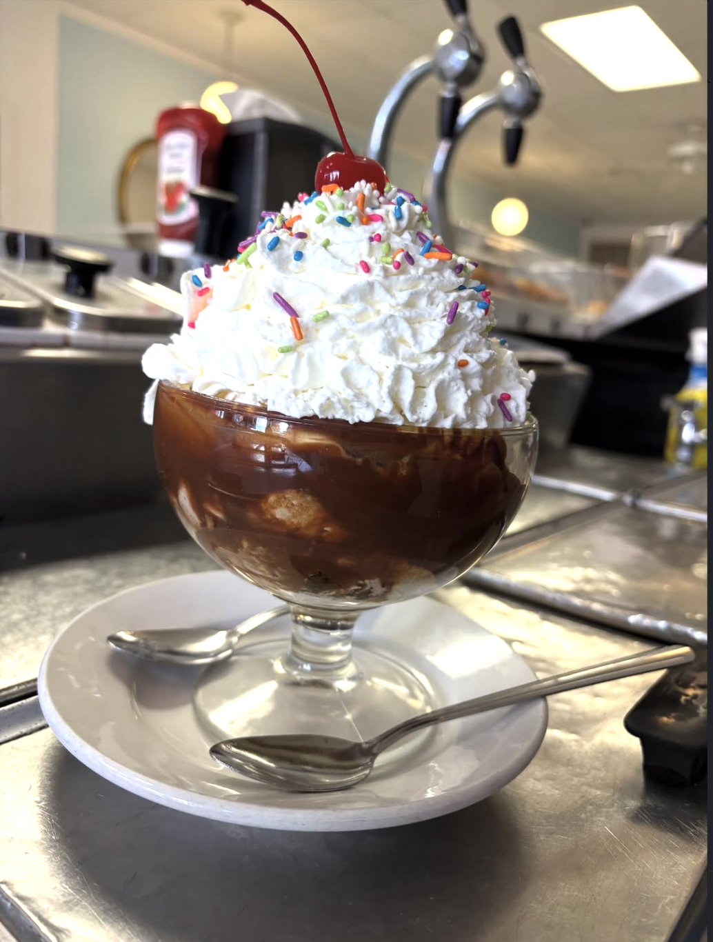 Hot fudge sundae with whipped cream, rainbow sprinkles, and a cherry on top