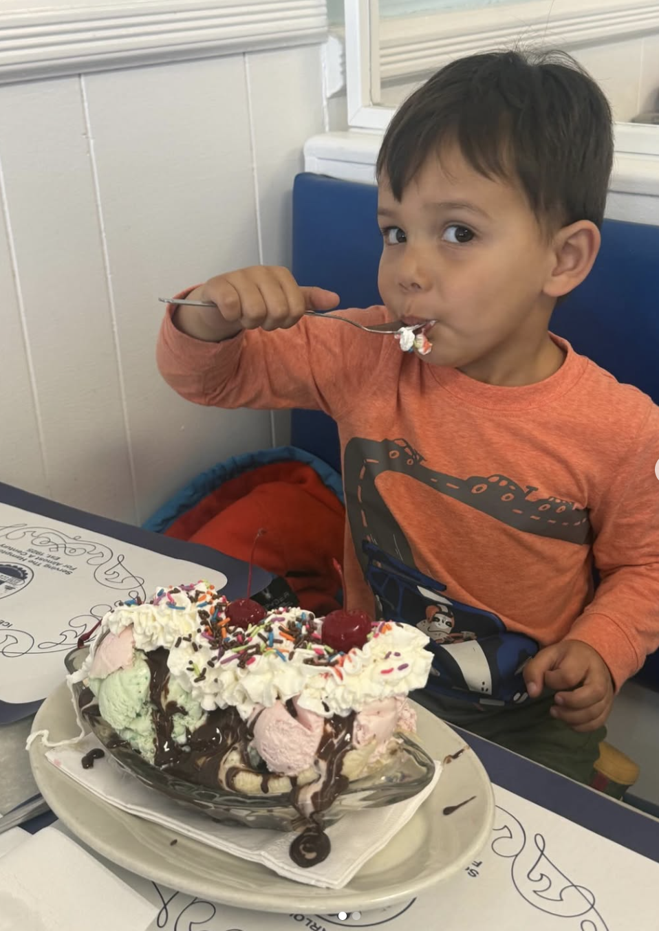 Little boy in a booth devouring a giant rainbow-sprinkle sundae